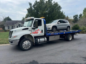 A Tow X flatbed tow truck transporting a silver SUV in a residential area in Greensboro, NC.