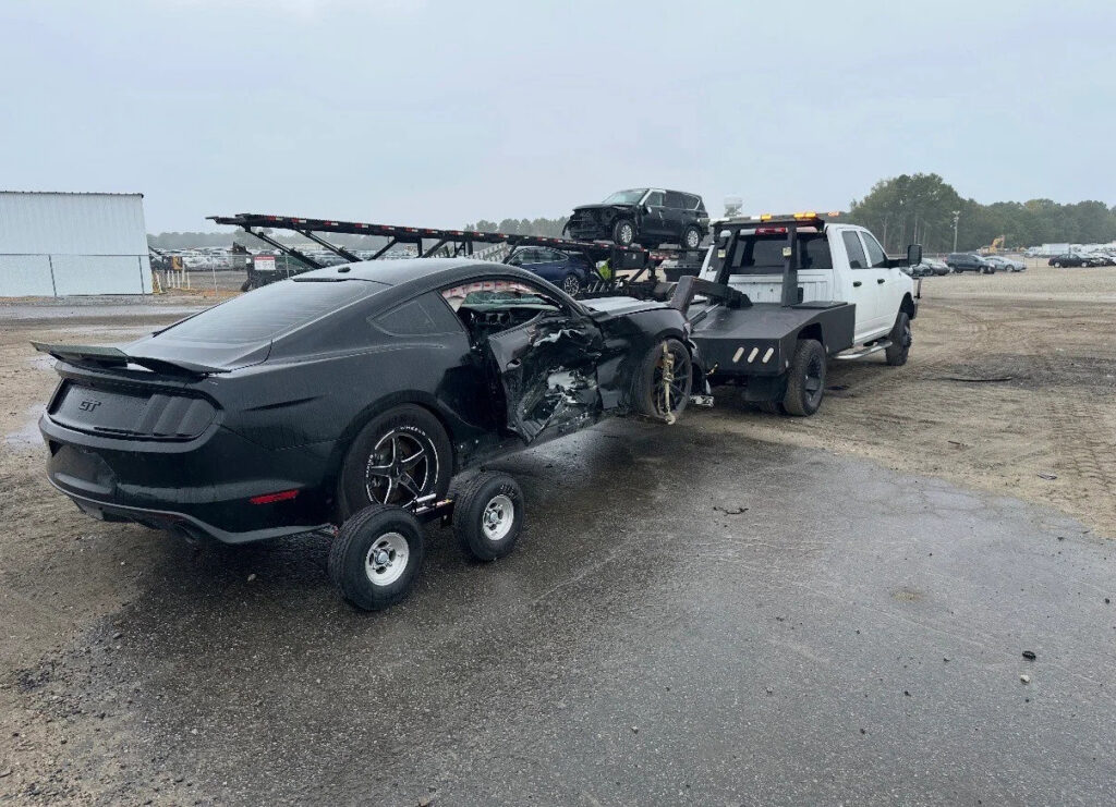 A Tow X truck towing a heavily damaged black Mustang with a dolly in Greensboro, NC.