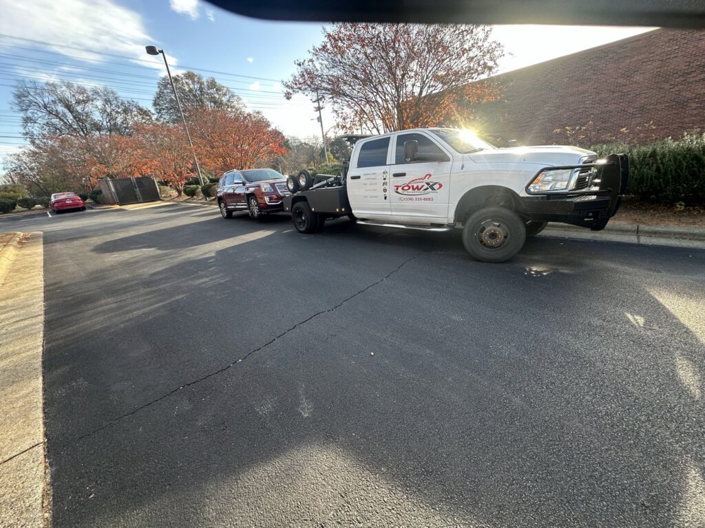 A Tow X truck towing a red SUV with a dolly in a parking lot in Greensboro, NC.
