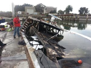 TowBoatUS San Diego crew salvaging a heavily damaged boat partially submerged at a dock in San Diego, CA.