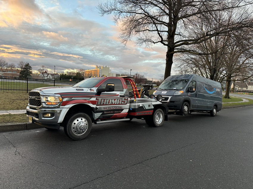 Thomas Towing & Recovery truck towing a grey Amazon delivery van in Newark, NJ.