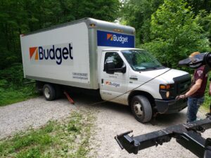 A TowTime Towing and Recovery truck preparing to tow a Budget box truck from a dirt path in Bloomington, IN.