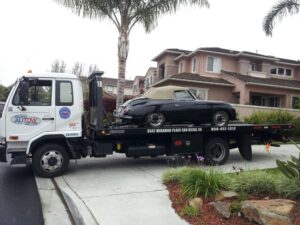 A Pacific Autow Center tow truck transporting a black classic convertible car on its flatbed in San Diego, CA.