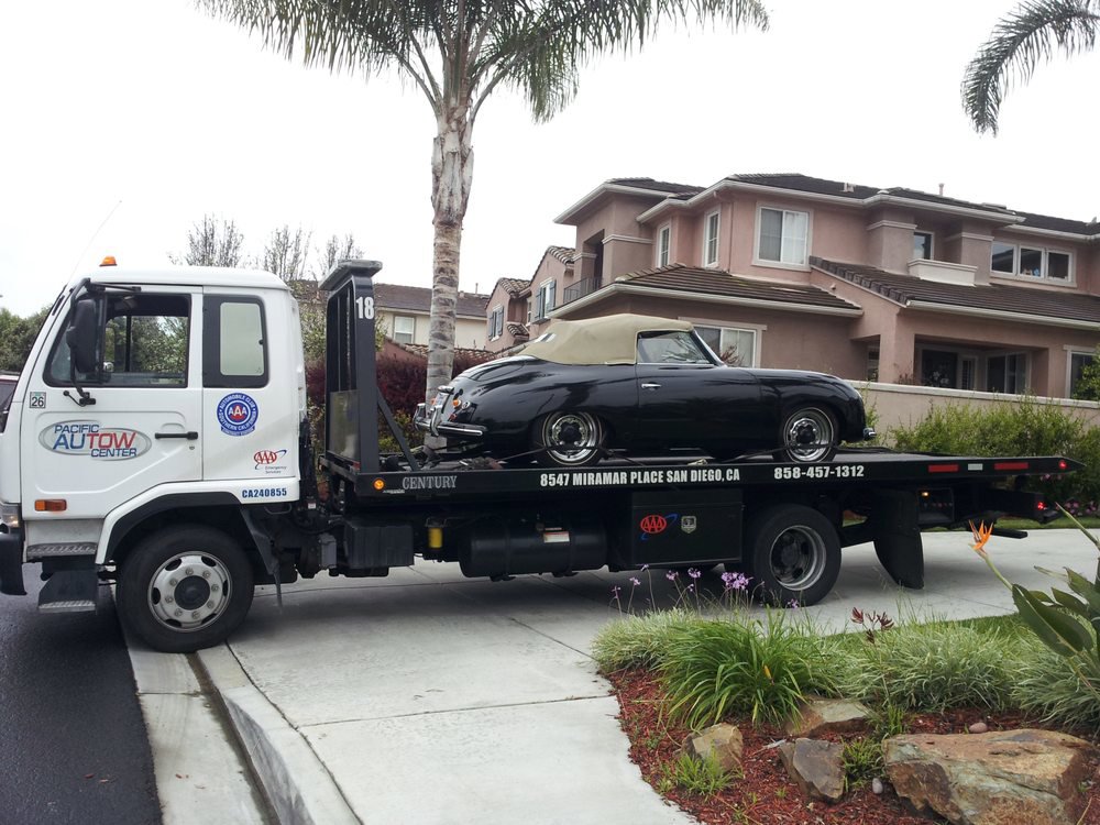 A Pacific Autow Center tow truck transporting a black classic convertible car on its flatbed in San Diego, CA.