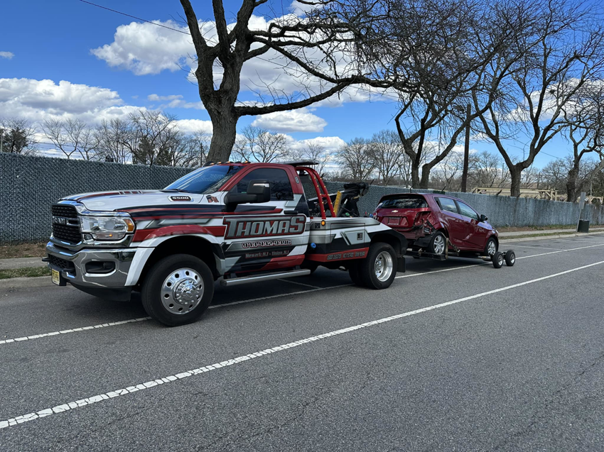 Thomas Towing & Recovery truck towing a damaged red car on dollies in Newark, NJ.