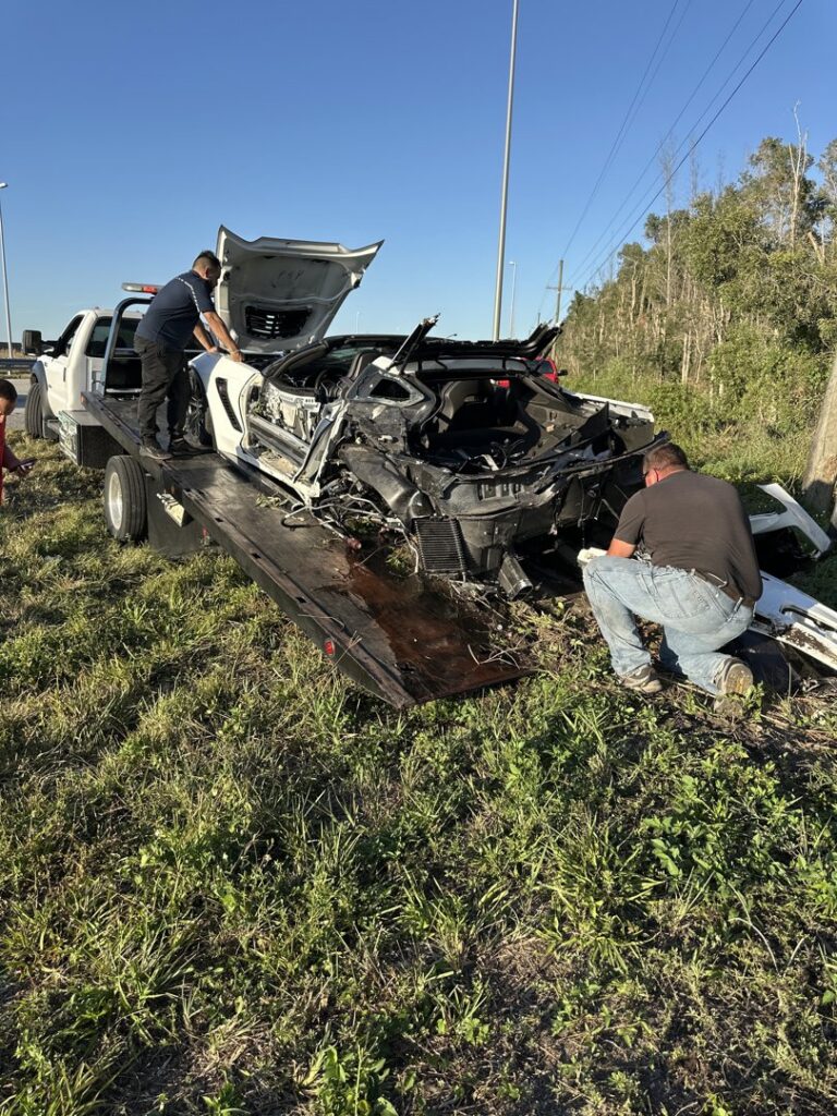 A tow truck from Rodicio Towing Services transporting a heavily damaged white sports car in Hialeah, FL.