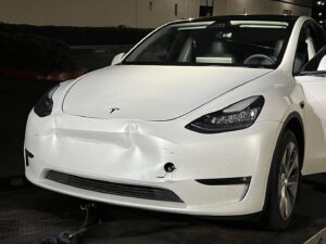 A Pacific Autow Center tow truck transporting a damaged white Tesla Model Y on its flatbed in San Diego, CA.