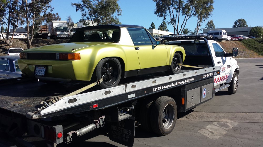 A Pacific Autow Center tow truck transporting a gold classic sports car on its flatbed in San Diego, CA.