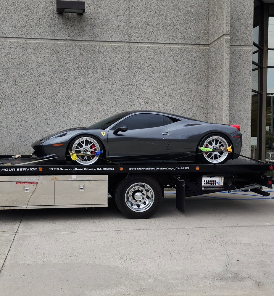 A Pacific Autow Center tow truck transporting a grey Ferrari sports car on its flatbed in San Diego, CA.