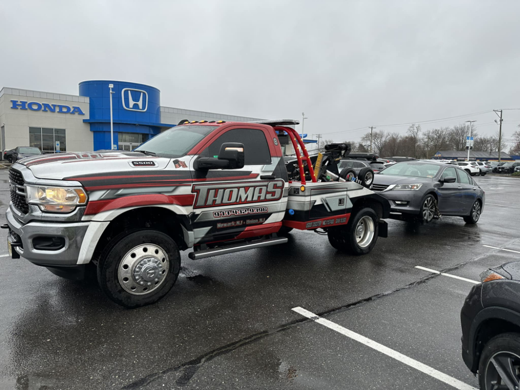 Thomas Towing & Recovery truck towing a grey sedan from a parking lot in Newark, NJ.