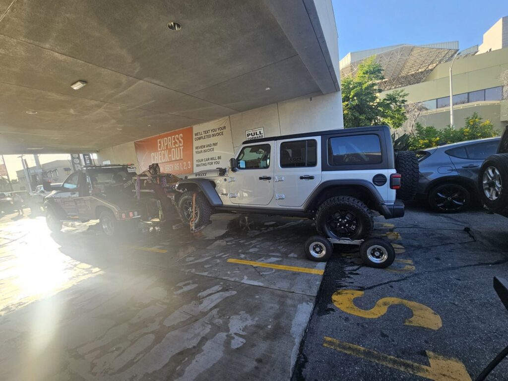 Orellanas Towing & Junk Car tow truck towing a white Jeep Wrangler using dollies in Los Angeles, CA.