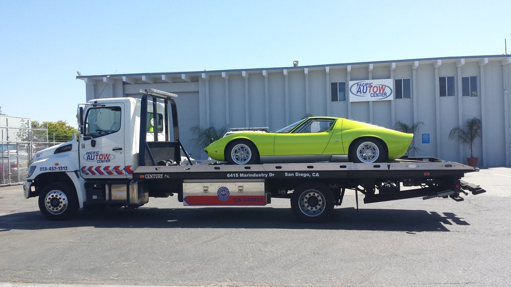A Pacific Autow Center tow truck transporting a lime green classic sports car on its flatbed in San Diego, CA.