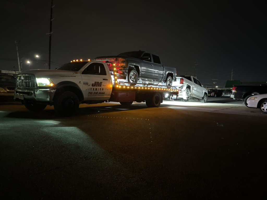 JM Towing & Transport LLC towing two pickup trucks at night in Houston, TX.