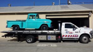 A Pacific Autow Center tow truck transporting a vintage turquoise pickup truck on its flatbed in San Diego, CA.