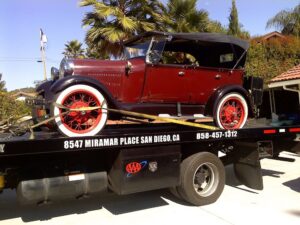 A Pacific Autow Center tow truck transporting a vintage red convertible car on its flatbed in San Diego, CA.