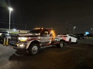 Thomas Towing & Recovery truck towing a white car on dollies at night in Newark, NJ.