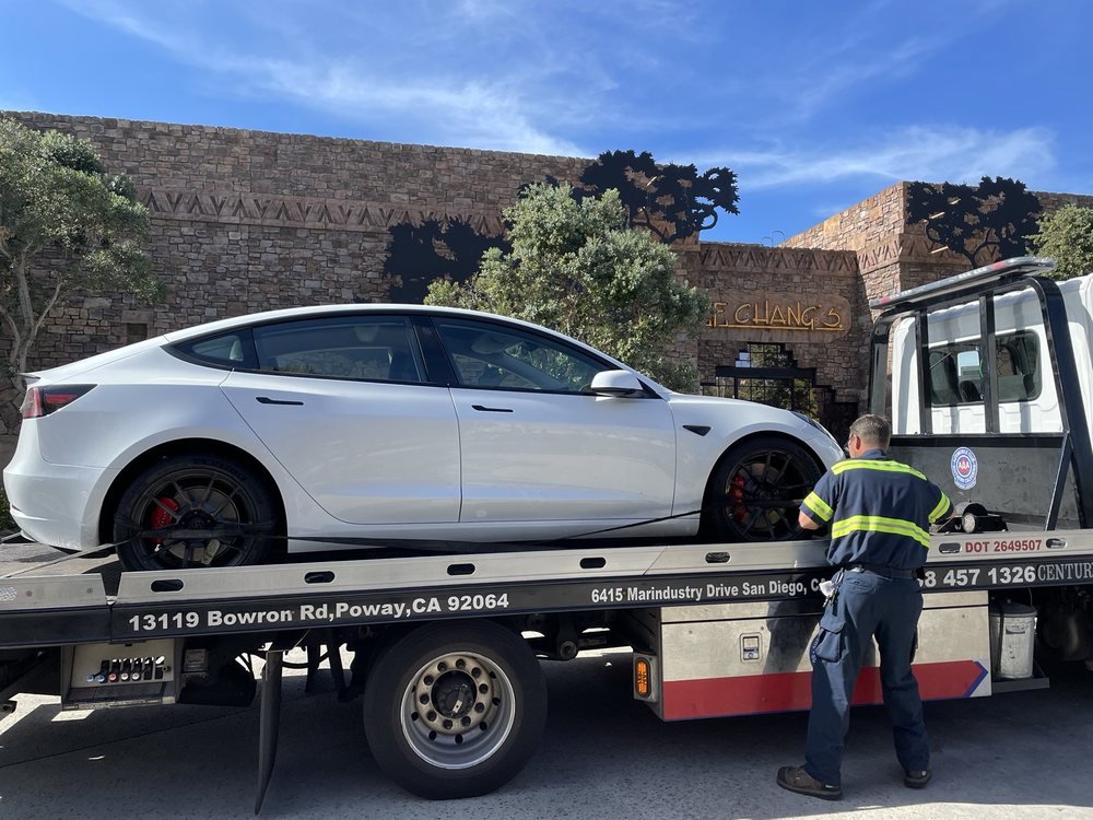 A Pacific Autow Center tow truck worker securing a white Tesla Model 3 on its flatbed in San Diego, CA.