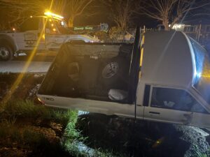 A white Toyota pickup truck stuck in a ditch at night, with a Kennedy Towing & Transport tow truck preparing for recovery in Anderson, CA.