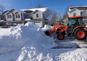 A tractor with a front-end loader clearing a large pile of snow in a residential area by TPM Snow Removal in Schenectady, NY.