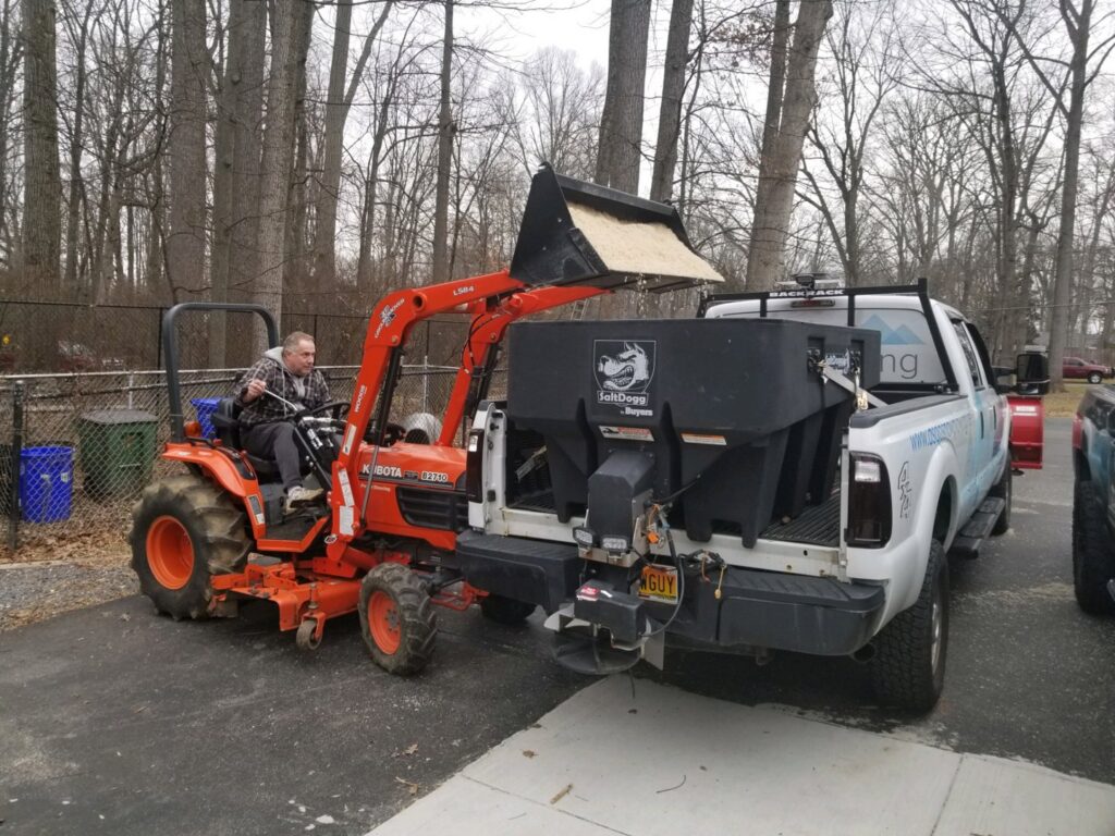 A tractor loading de-icing salt into a truck-mounted spreader for American Snow Plowing Services in Rockville, MD.