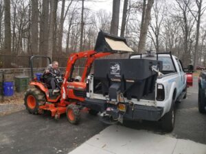 A tractor loading de-icing salt into a truck-mounted spreader for American Snow Plowing Services in Rockville, MD.