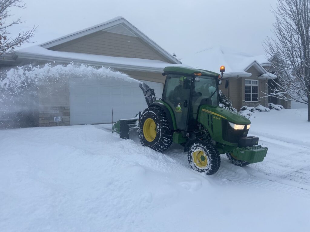A tractor with a snow blower attachment clearing a residential driveway for Rochester Ground Lawn & Snow Services in Rochester, MN.