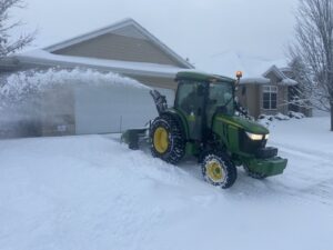 A tractor with a snow blower attachment clearing a residential driveway for Rochester Ground Lawn & Snow Services in Rochester, MN.