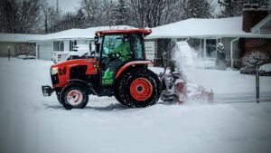 A JD Lawn Care LLC tractor with a snow blower clearing a residential driveway in Berea, OH.