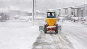A tractor equipped with a salt spreader applying material to a snowy road as part of snow management by JC Snow Management in Mount Vernon, NY