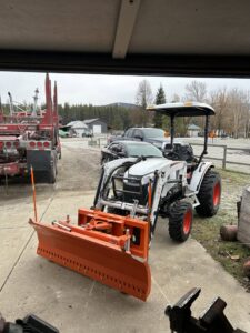 A white tractor with an orange snow plow attachment, ready for snow removal by Victory Tractor Implements in Long Beach, CA