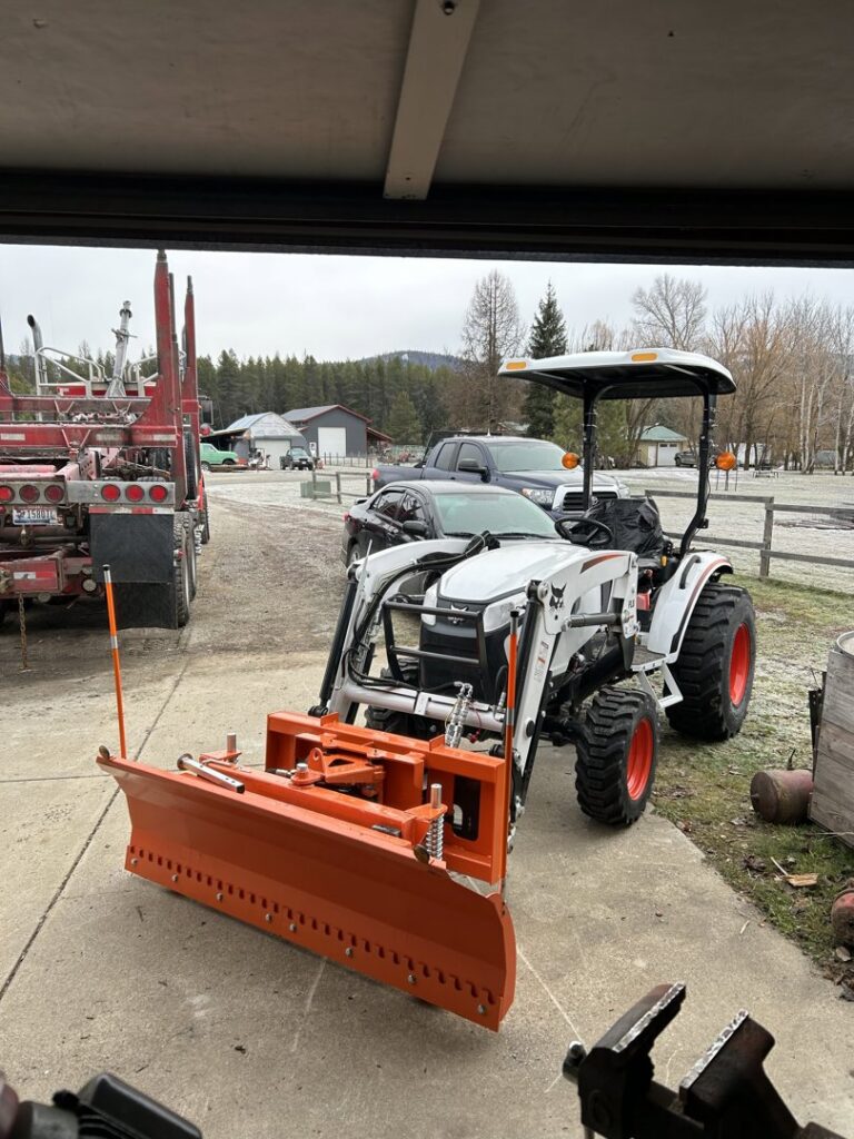 A white tractor with an orange snow plow attachment, ready for snow removal by Victory Tractor Implements in Long Beach, CA