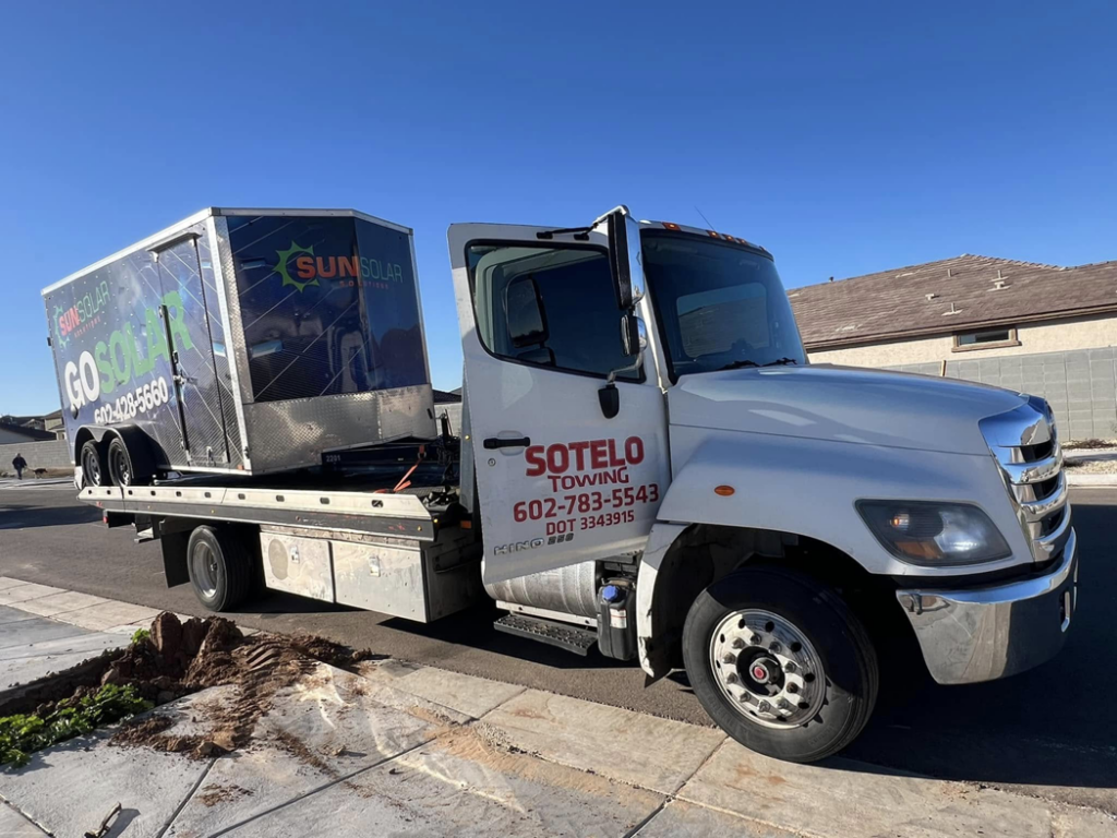 Sotelo Towing LLC transporting a large SunSolar branded trailer on a flatbed tow truck in Phoenix, AZ.