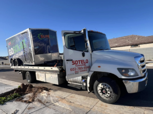 Sotelo Towing LLC transporting a large SunSolar branded trailer on a flatbed tow truck in Phoenix, AZ.