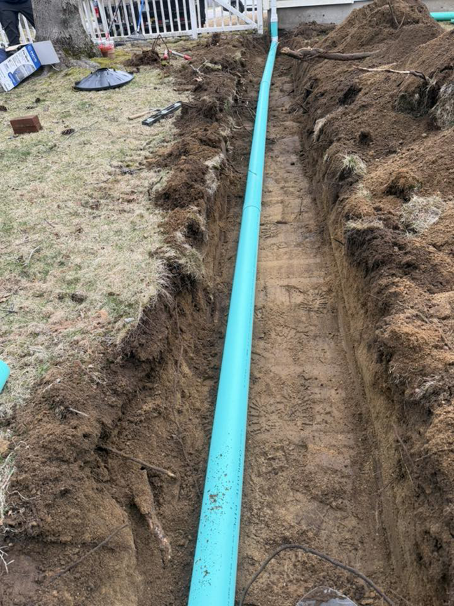 A trench with a blue drainage pipe being installed by Fleury Dirt Works & Services Llc in Cumberland, RI