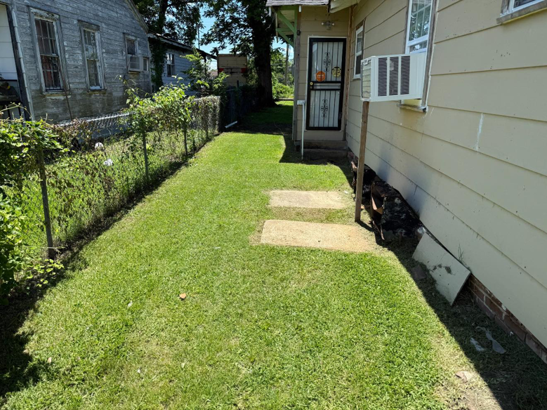 A neatly trimmed side yard with green grass along a chain-link fence, cared for by Day One Landscaping in Mississippi.