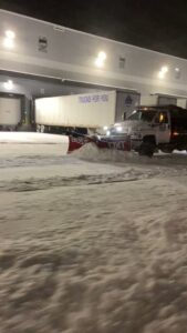 A snow plow truck actively clearing snow from a commercial lot at night by Turf Pro Lawn Care & Snow Removal in Green Bay, WI.