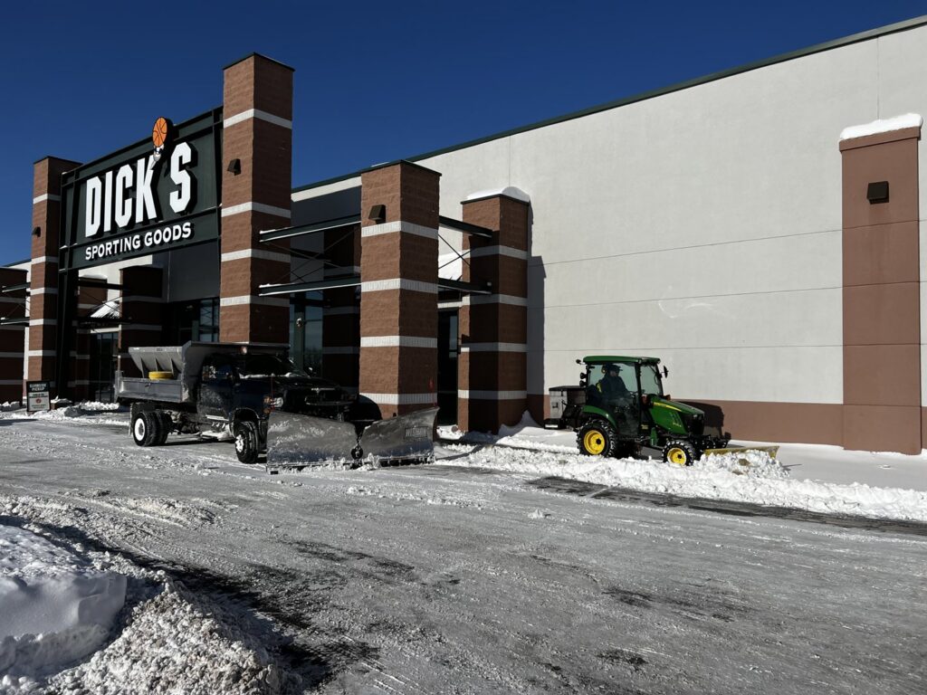 A snow plow truck and a small tractor plowing snow in front of Dick's Sporting Goods for Appleton Snow Removal in Appleton, WI.