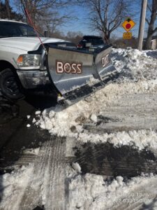 A white pickup truck with a BOSS DXT snow plow clearing snow from a street or large driveway by Diamond Image in New Haven, CT.