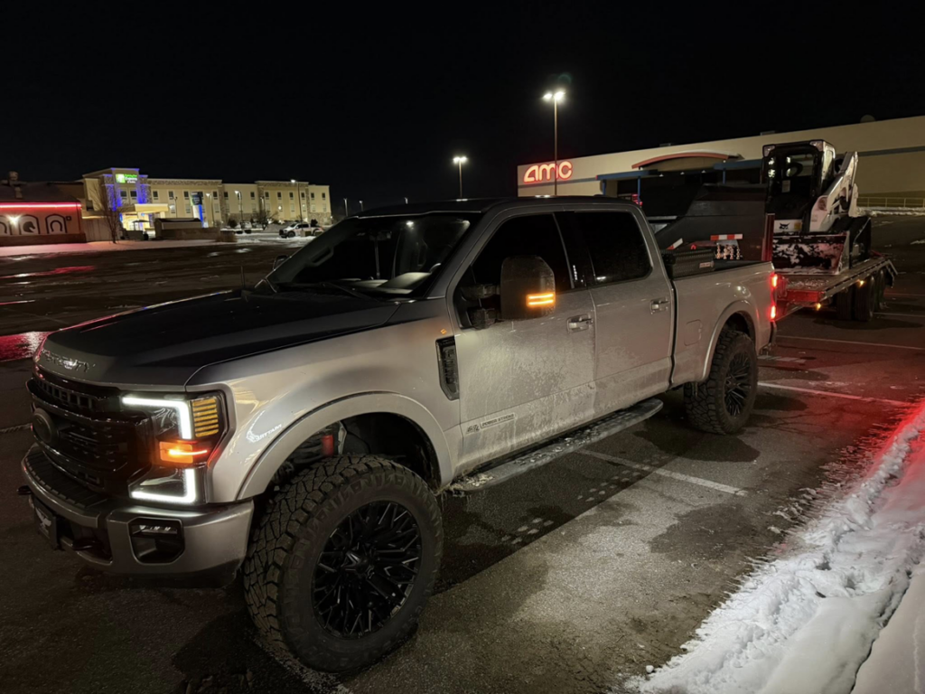 A large pickup truck towing a skid steer loader for snow removal services by Patriot Lawn and Landscaping LLC in Manassas, VA.