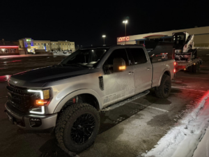 A large pickup truck towing a skid steer loader for snow removal services by Patriot Lawn and Landscaping LLC in Manassas, VA.
