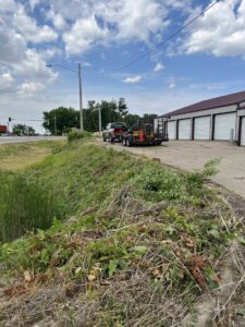 A truck and trailer with lawn care equipment parked next to an overgrown area, ready for clearing by Thompson Acres in Davenport, IA.