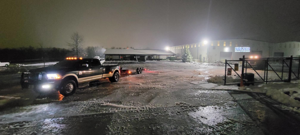 A Yard Monkeys truck with a trailer in a snowy parking lot at night, ready for snow removal in Hixson, TN.