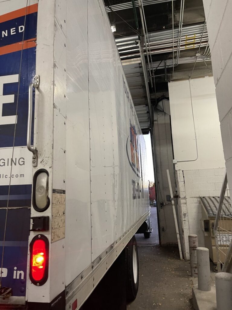 A TruMoving truck navigating a tight loading dock area at a business location in Lakewood, CO.