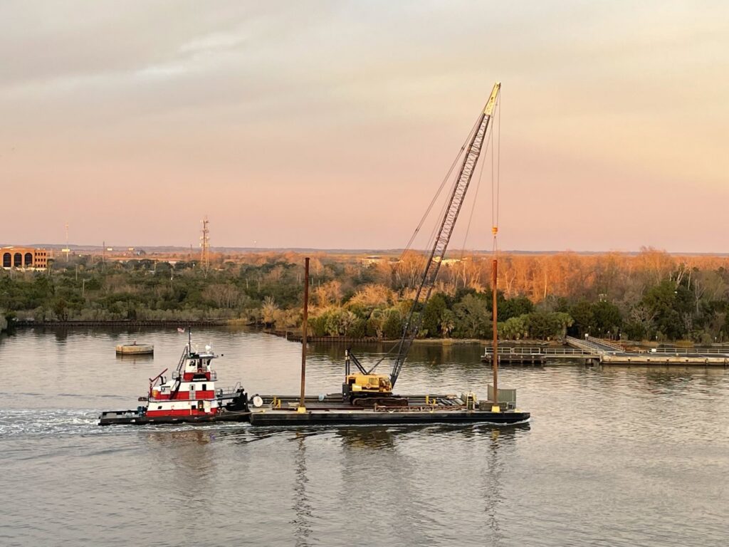 A tugboat from Myrick Marine Contracting Corp. in Norfolk, VA, towing a crane barge at sunset.