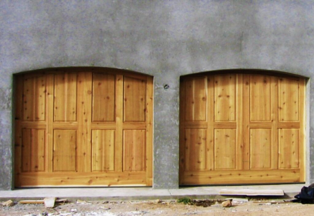 Two newly installed arched wooden garage doors on a building by Mark's Garage Door Services in Santa Fe, NM.