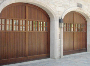 Two arched wooden garage doors with windows on a stone house, installed by K & B Door Co. in Las Vegas, NV