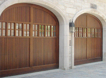 Two arched wooden garage doors with windows on a stone house, installed by K & B Door Co. in Las Vegas, NV