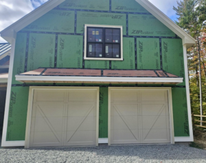 Two light beige carriage-style garage doors installed on a new construction building by Champion Overhead Door in Brattleboro, VT.