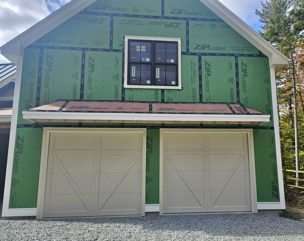 Two light beige carriage-style garage doors installed on a new construction building by Champion Overhead Door in Brattleboro, VT.