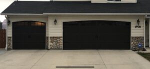 Two black garage doors with arched windows installed on a residential house by Overhead Door Company of Nampa in Nampa, ID.